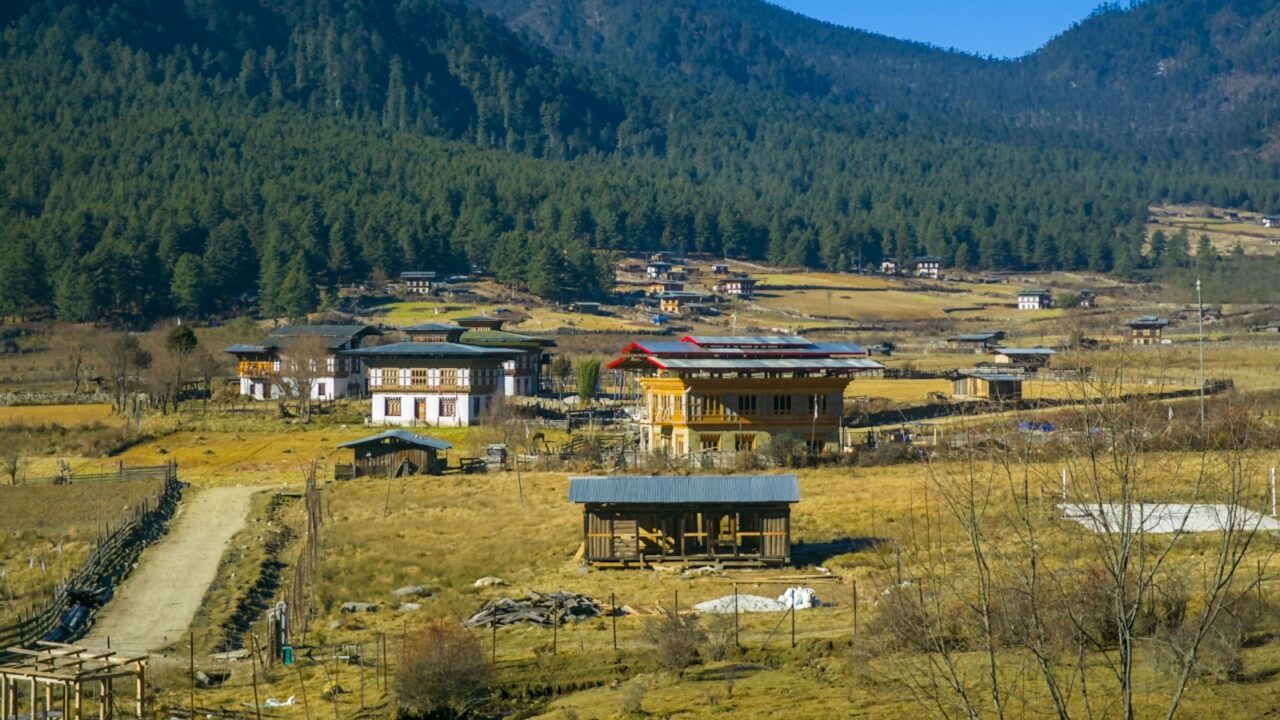 Scenic Phobjikha Valley landscape with traditional Bhutanese houses scattered across golden fields surrounded by dense forested mountains in central Bhutan