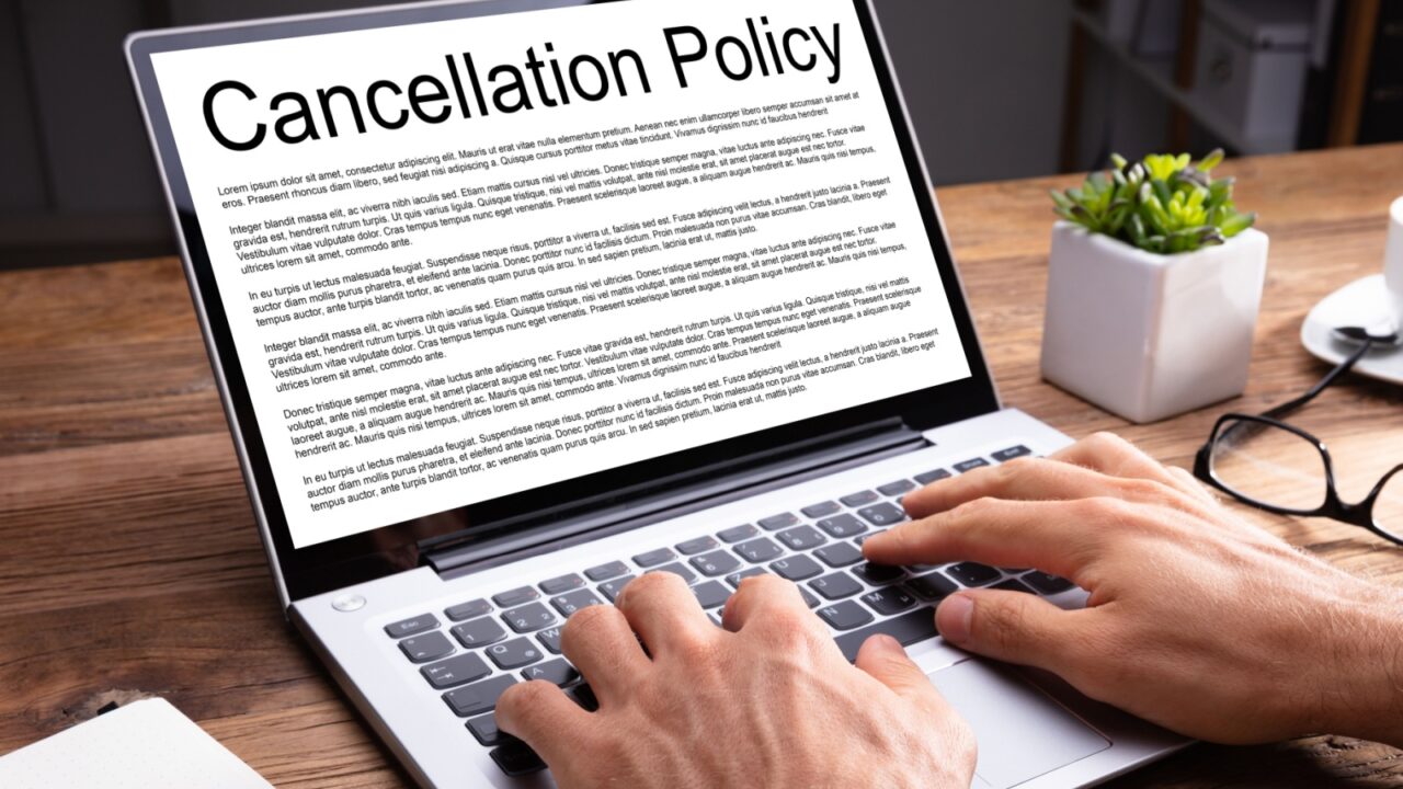 Man Reading Agreement Of Cancellation Policy On Laptop Screen Over Wooden Desk At Office