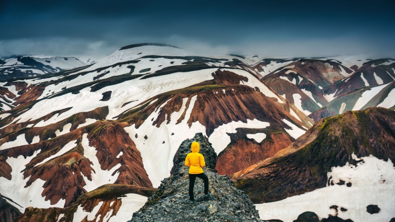 Hiker woman standing on peak of volcanic mountain with snow covered on Blanhjukur trail in summer at Landmannalaugar, Iceland