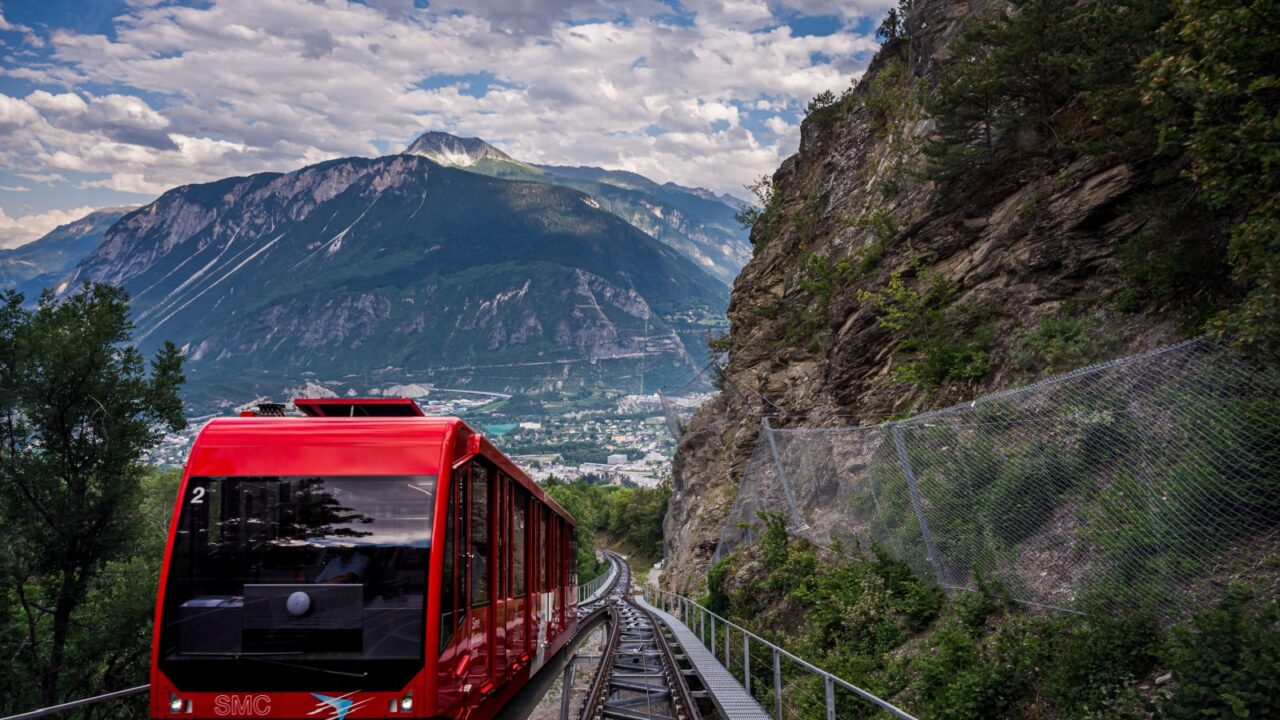 Crans Montana, Valais Canton, Switzerland - 15 July 2023: One red Swiss funicular from Sierre to Crans Montana. Public transport cable railway with scenic view over the city and mountain.