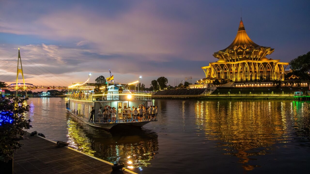SARAWAK, MALAYSIA - SEPTEMBER 16, 2023: Sarawak River Cruise boat with a background of State Legislative Assembly building during a sunset cruise. One of the popular tourist attractions in Kuching.