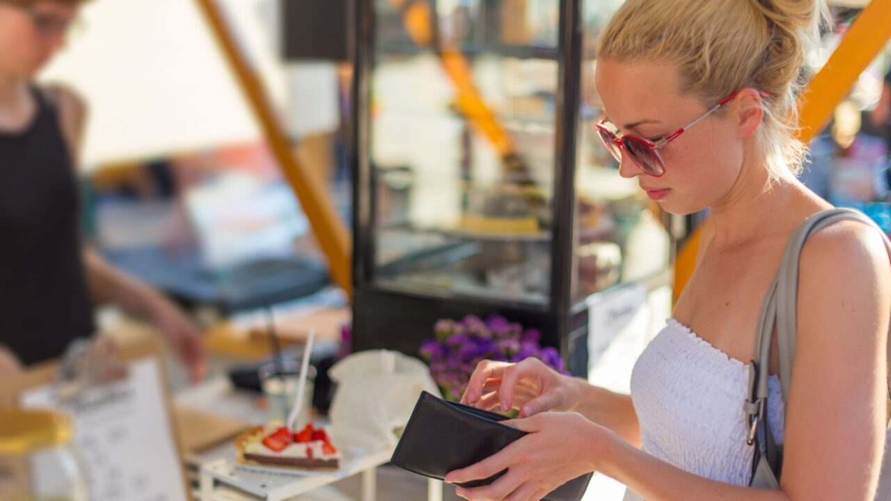 Beautiful blonde caucasian lady wearing white summer dress buying freshly prepared meal at a local street food festival. Urban international kitchen event in Ljubljana, Slovenia, in summertime.