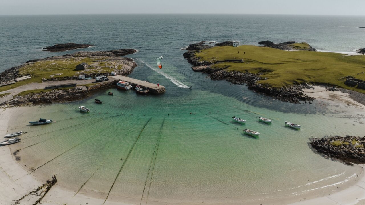 An aerial view of a kite surfer in water along Tiree island in Scotland with a sandy beach and seascape in the background