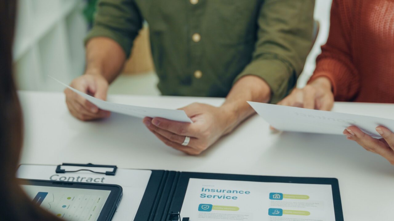 Close-up of Asian couple checking insurance documents and financial contract during advisor meeting. Concept of finance, investment, and agreement approval.