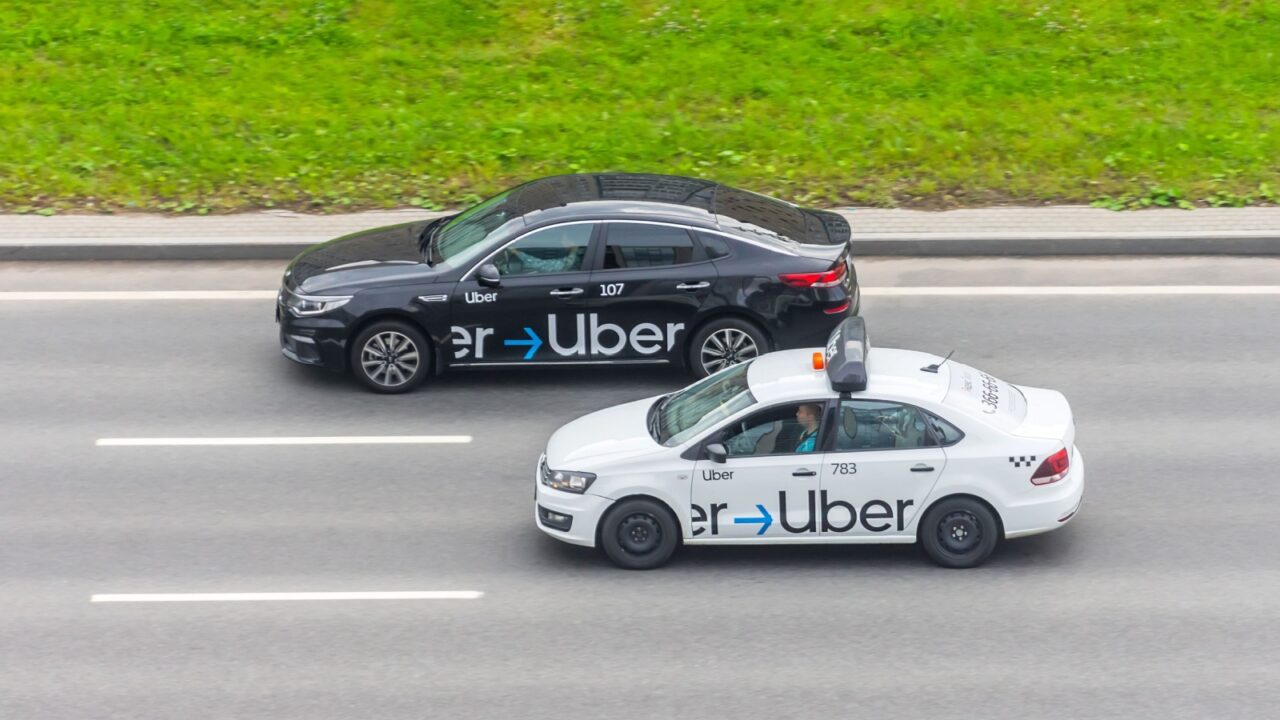 White and black passenger car Uber Taxi rides on the highway aerial view. Russia, Saint-Petersburg. 30 august 2020.