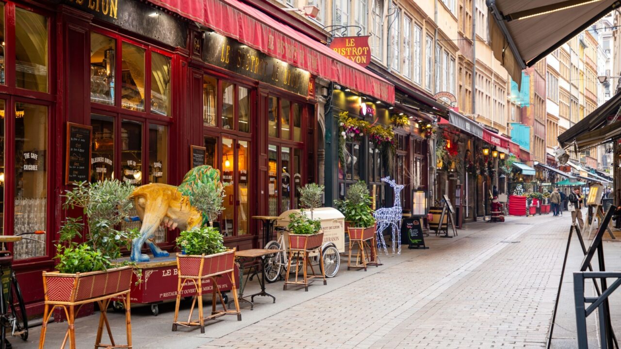 Colorful French bistro street with red awnings, festive decorations, outdoor seating, and cobblestone charm.