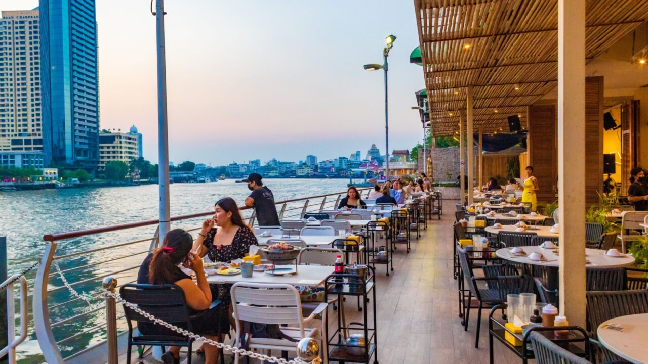 Bangkok,Thailand-May 02 2024:Riverside buildings and River city pier- starting point for cruises on the Chao Phraya River with panoramic views of the illuminated city,its skyscrapers and temples