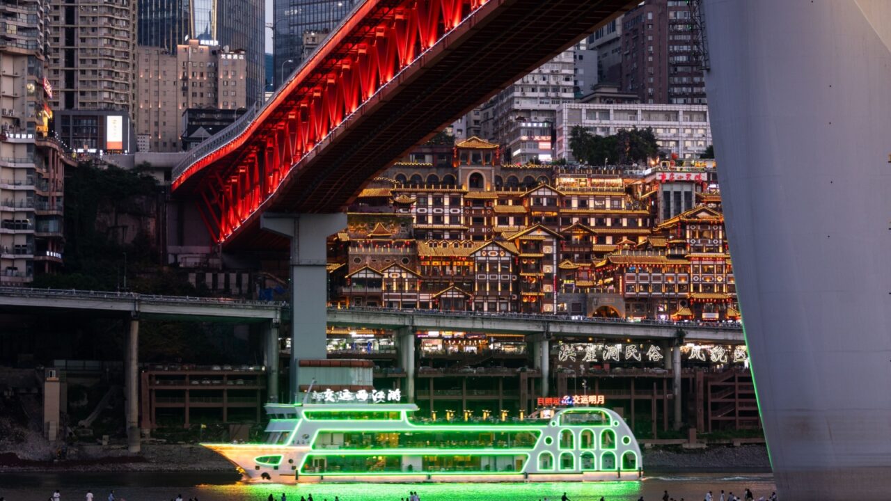 Chongqing, China - May 10 2025: An illuminated cruise ship sails in front of the famous Hongya Cave scenic area along the Yangtse river in Chongqing