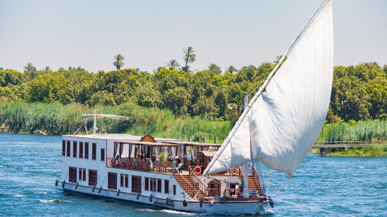 Elegant cruise ship with white sail is sailing on the calm waters of the river Nile, Egypt. Blue rippled waters on the foreground.