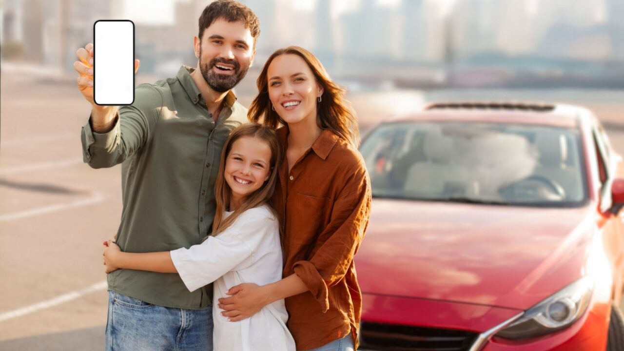 Online car insurance. European family with child standing near new auto and showing smartphone with blank screen, recommending mobile application, mockup