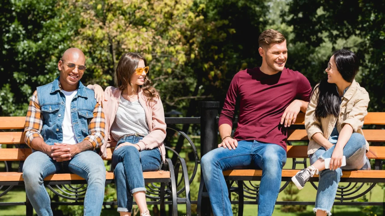 cheerful multicultural friends smiling while sitting on benches in park