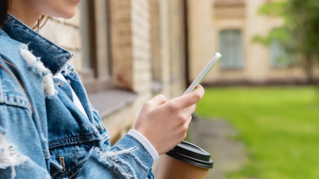 cropped view of cheerful student using smartphone and holding paper