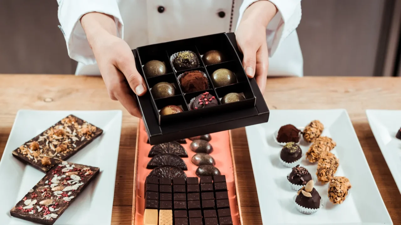 cropped view of chocolatier holding box with fresh made chocolate
