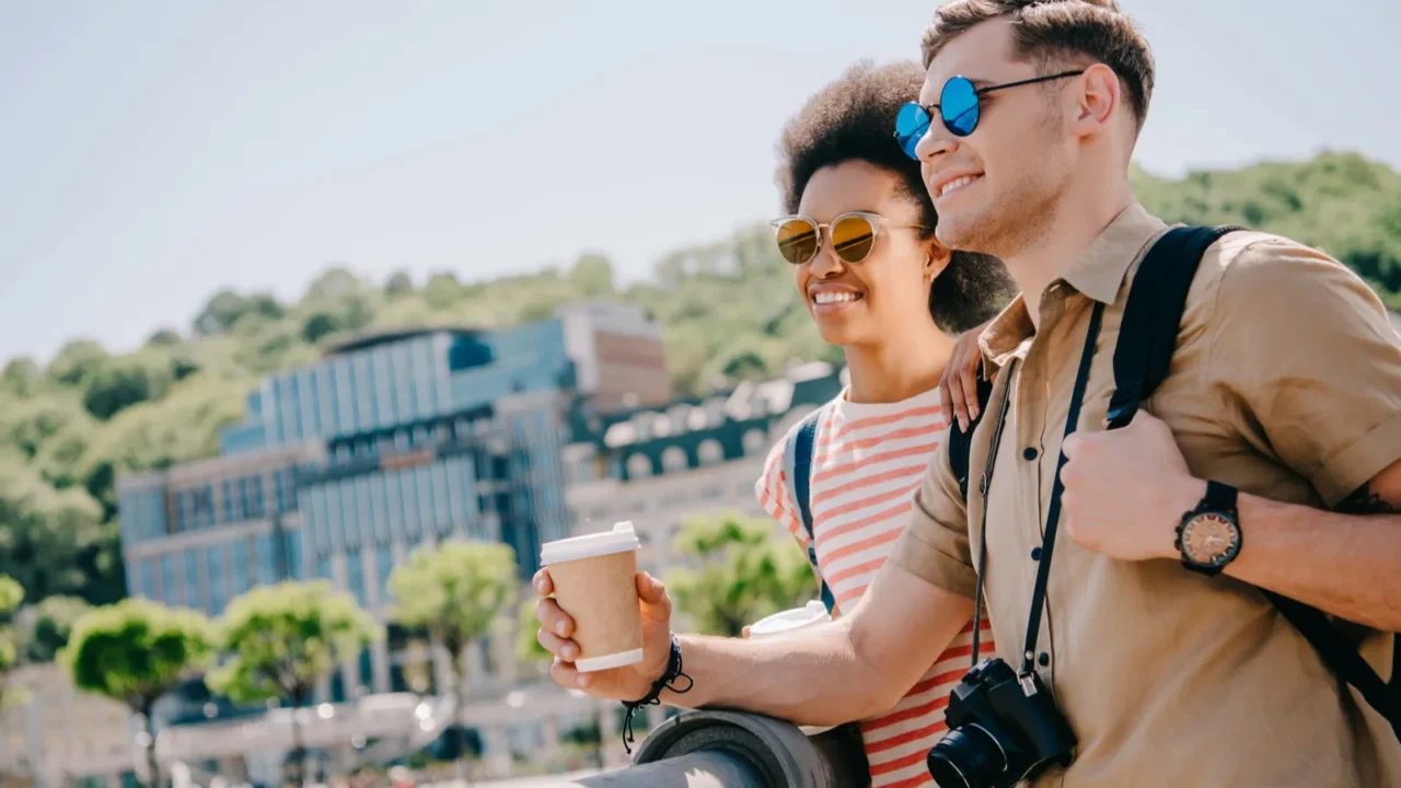 smiling interracial couple of tourists in sunglasses with coffee and