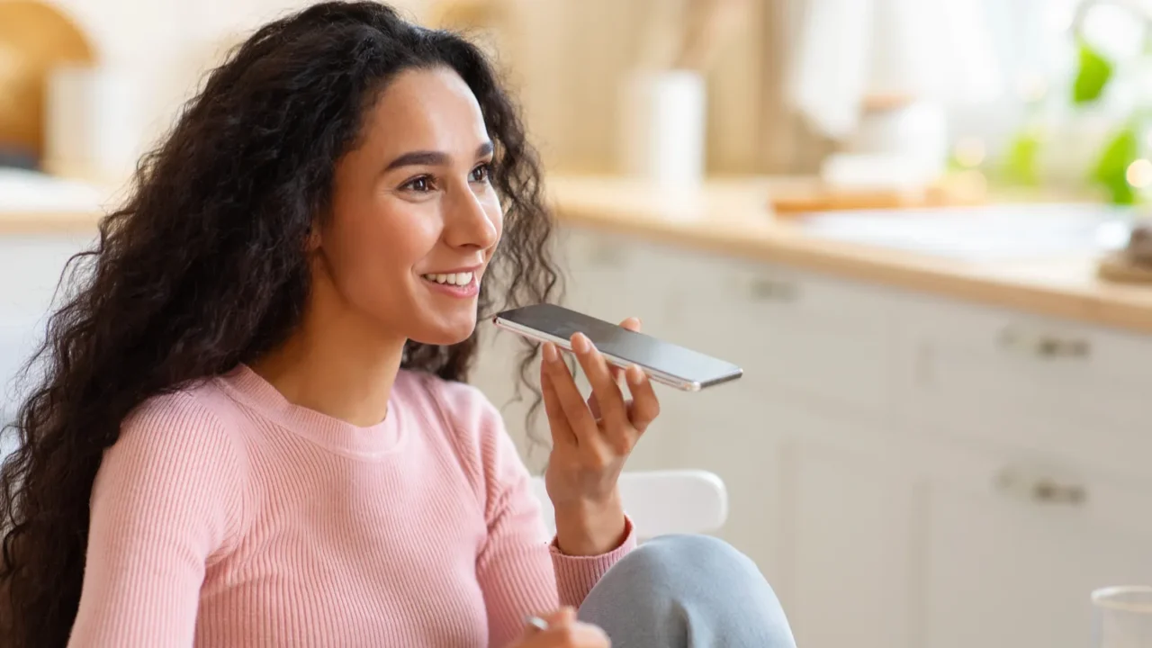 smiling young woman with smartphone sending audio messages while having