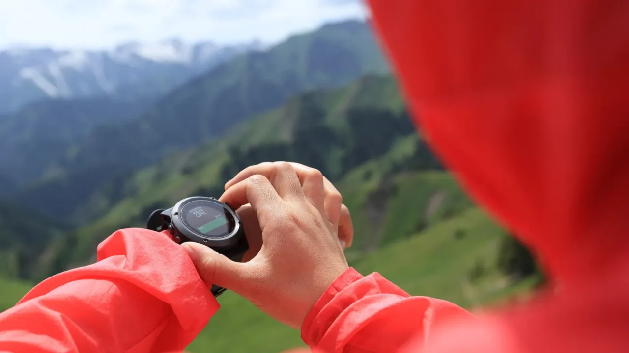 Young woman hiker checking the altimeter on sports watch at mountain peak