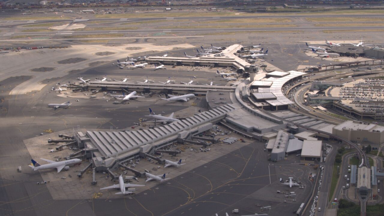 AERIAL, CLOSE UP: Flying above airplanes parked on apron waiting for passengers to board through jetway and start their traveling journey. Terminal building on New York Newark international airport