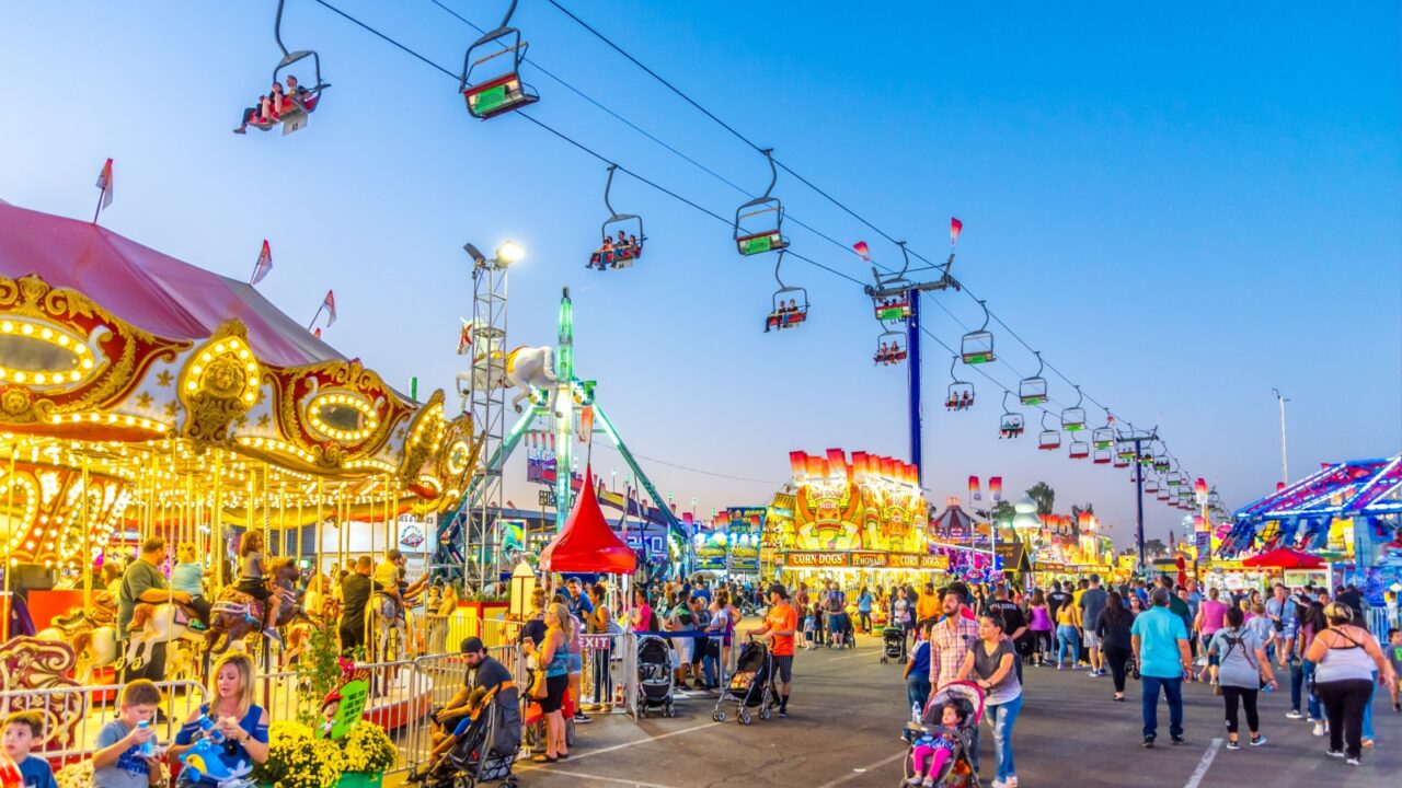 Phoenix, Arizona - October 25, 2017: Guests in ski chairs pass over the colorful, crowded midway of the Arizona State Fair during the early evening hours.