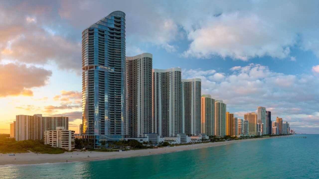 Evening landscape of sandy beachfront in Sunny Isles Beach city with luxurious highrise hotels and condo buildings on Atlantic ocean shore. American tourism infrastructure in southern Florida