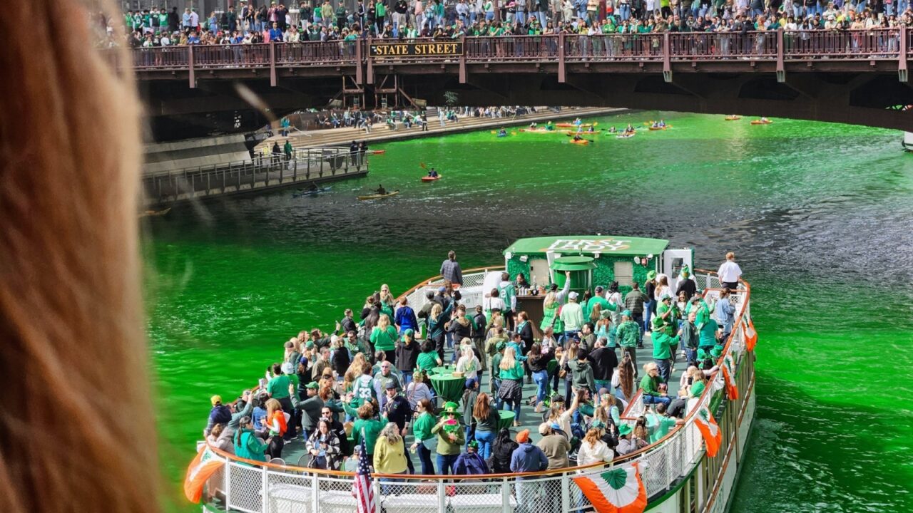 Chicago, Illinois, USA - March 15, 2025: POV from bridge of St. Patrick's Day celebrations with packed boat passing by in green-dyed Chicago River and crowded bridge.