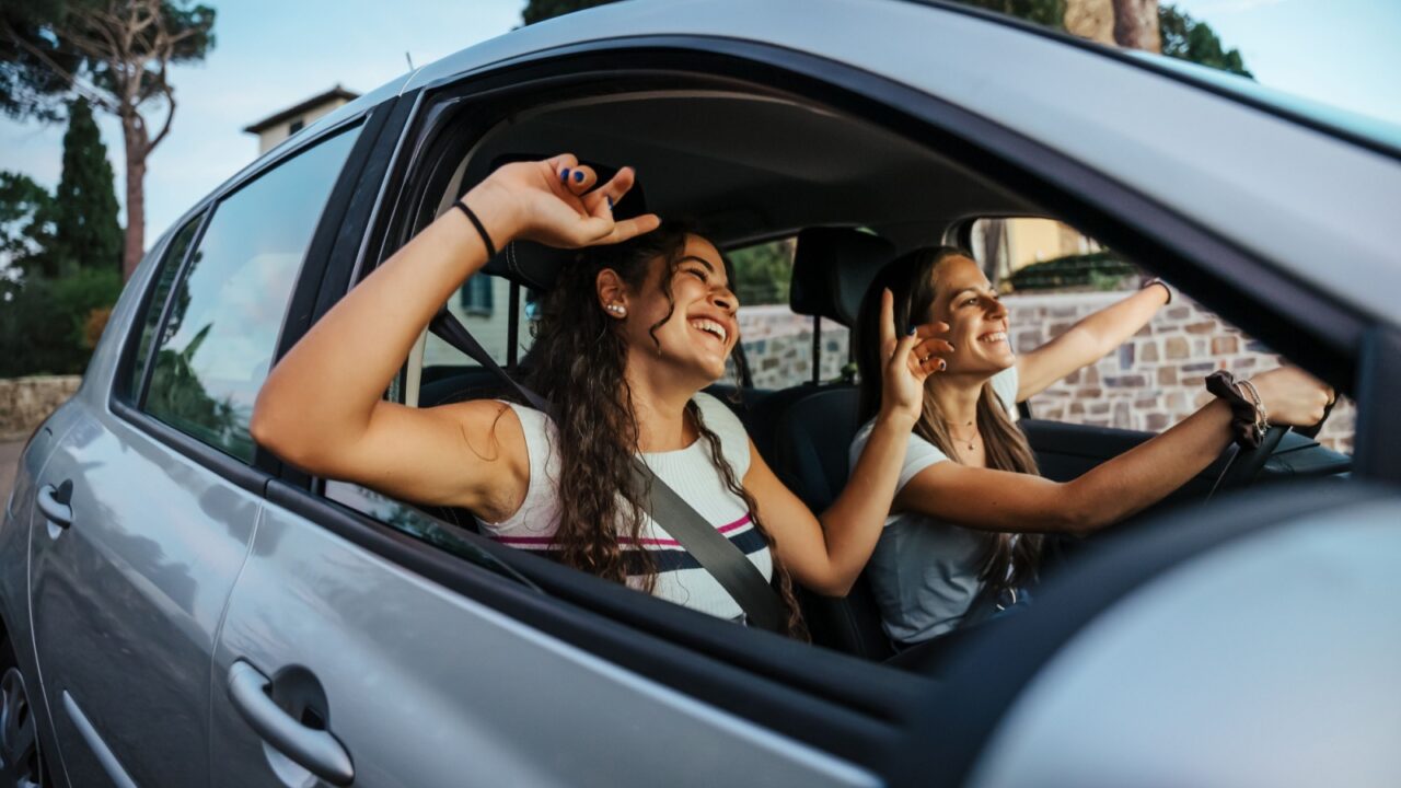 Two young women sing a song on the radio and dance in the car on a day trip in the summer