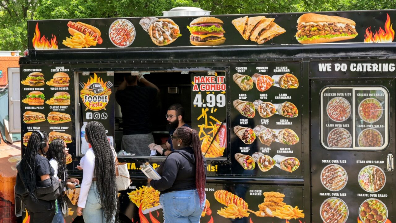 People buying fast food from a mobile food truck parked on one of the main roads in Washington DC See less
