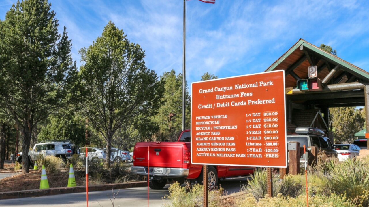 Grand Canyon, AZ - November 10, 2017: View of cars arriving at Grand Canyon National Park South Rim toll booths, entrance fees sign and US flag in the background. Photo taken on a sunny day.