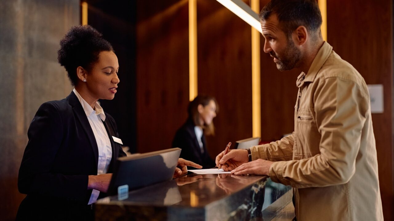 African American female receptionist assisting a guest with filling out documents while checking in at the hotel.
