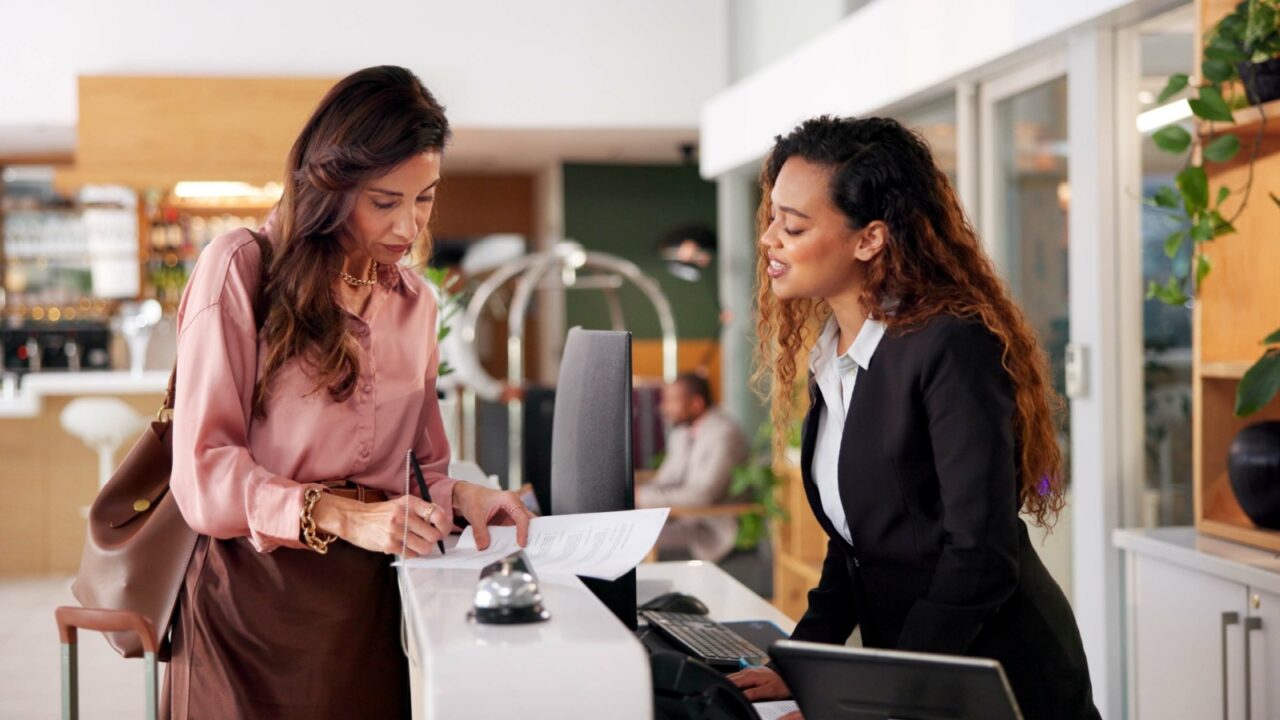 Hotel, lobby and woman with documents for receptionist for booking, guest room service and reservation. Hospitality, front desk and person with concierge for check in, accommodation and sign forms