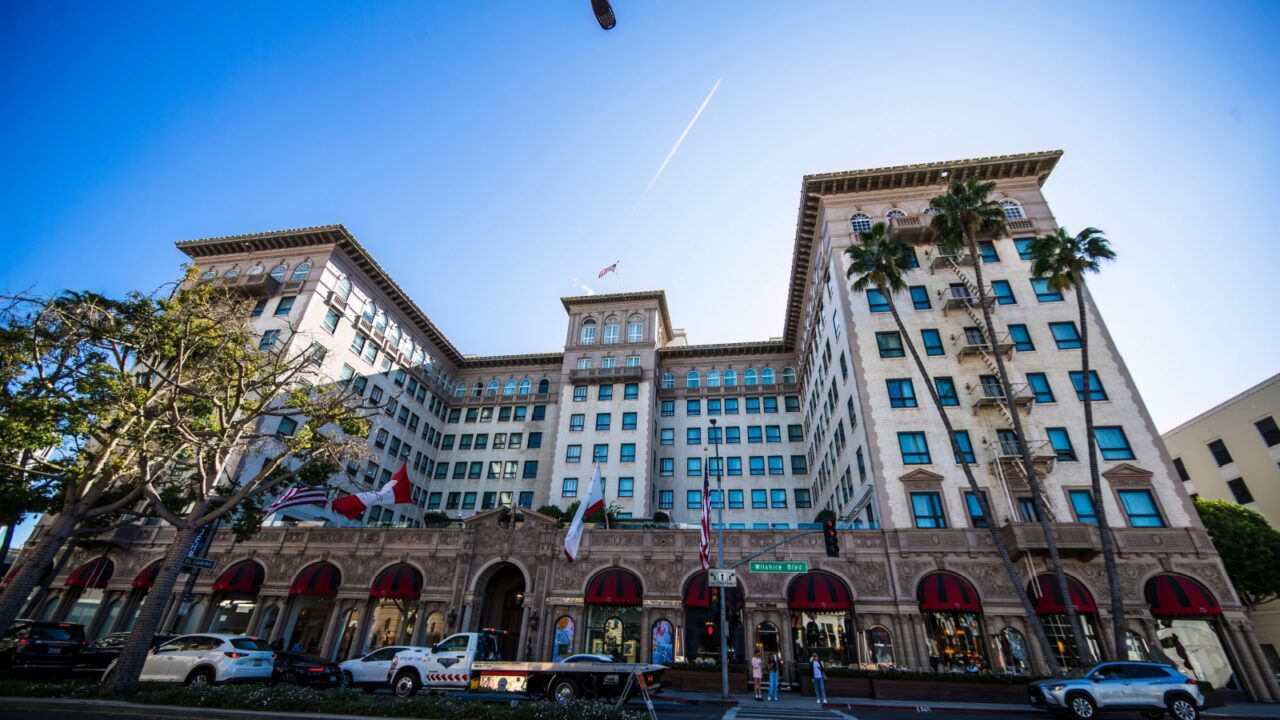 2024-11-15 Los Angeles USA The Beverly Wilshire, A Four Seasons Hotel, a grand historic building with arched windows, palm trees, and international flags on a sunny urban street.