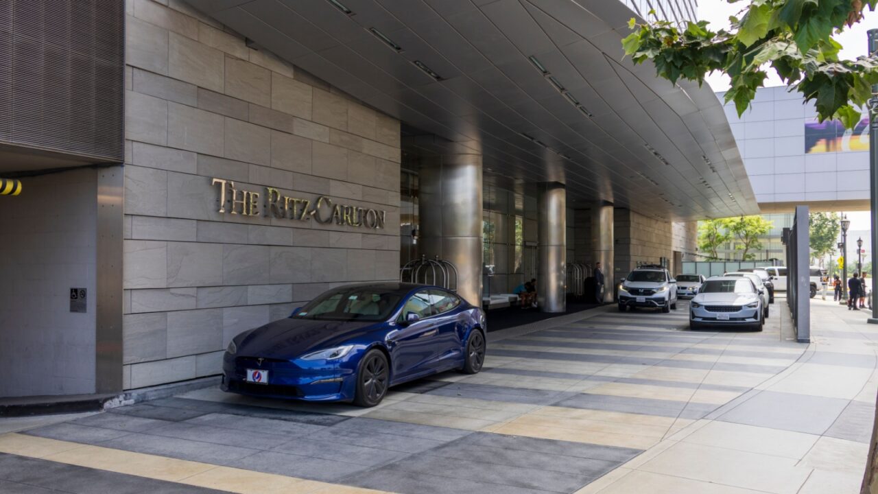 Los Angeles, California USA - 7 22 2023: The Ritz Carlton Hotel with a blue Tesla Model S and other cars parked in front and people standing on the sidewalk in Los Angeles California USA