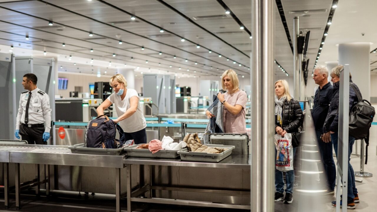 Istanbul, Turkey - February 21, 2020 - Passengers at an airport security checkpoint, placing belongings in trays for inspection while a security officer oversees the process.