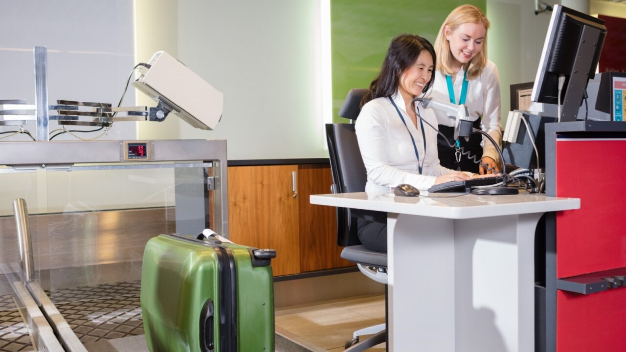 Staff Weighing Luggage At Airport Check-in Desk