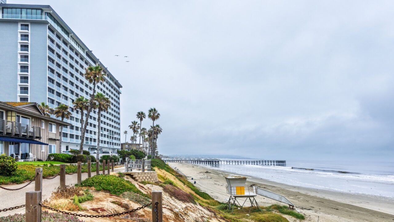 Coast of North Pacific Beach lined up with multitude of small and big resort hotels with distant view of public historic wooden Crystal Pier, San Diego, CA