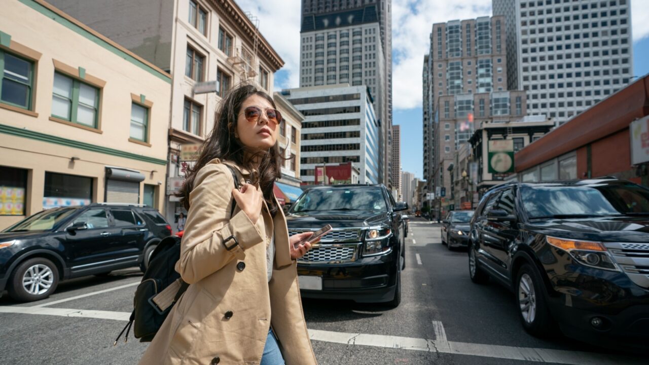 fashionable asian Taiwanese woman tourist passing by cars as she's crossing the road during her visit in downtown san Francisco California usa. she looks into distance while walking