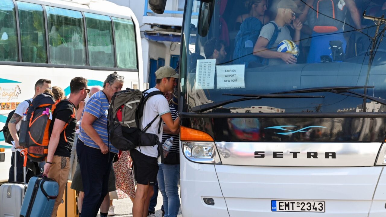 Mykonos, Greece - June 2022: People crowding to get onto the airport shuttle bus in the town's bus station on the Greek Island of Mykonos.