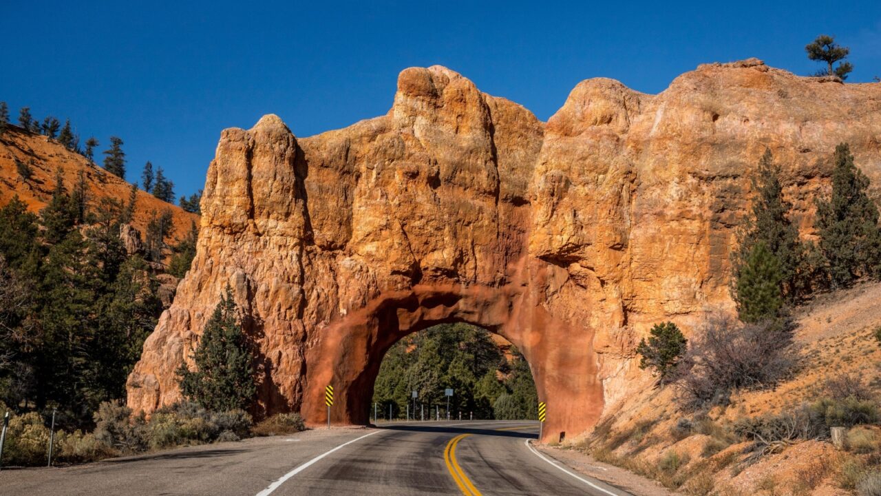 Discover the scenic beauty of Panguitch, Utah, where a winding road passes through a stunning sandstone arch surrounded by nature.