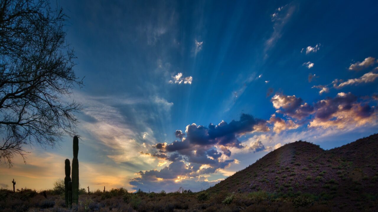 A desert sunset in Scottsdale, Arizona highlighted by sunday's and clouds with saguaro cactus silhouettes.