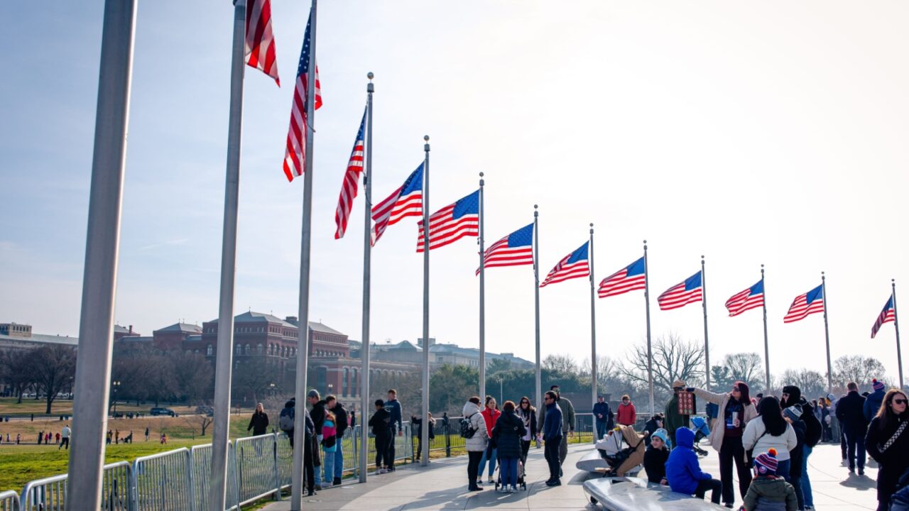 Washington DC, US - December 27, 2024: tourists and visitors by the flags at The Washington Monument, an obelisk on the National Mall in Washington, D.C., built to commemorate George Washington