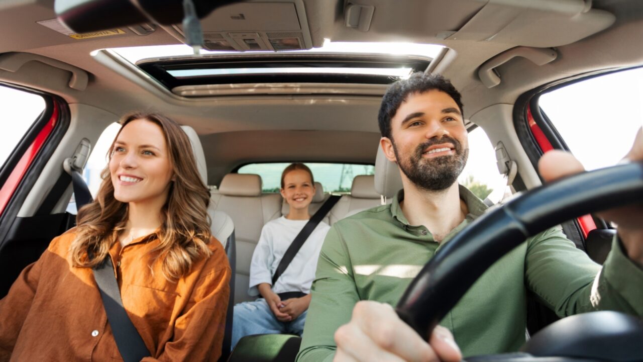 Happy parents with child daughter riding car, traveling by automobile together, family of three enjoying road trip