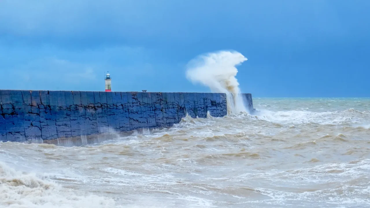a harbour wall with a rough sea crashing against it