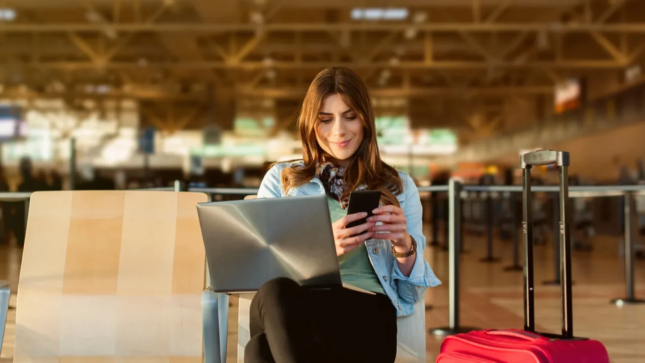 female passenger on smart phone and laptop sitting in terminal