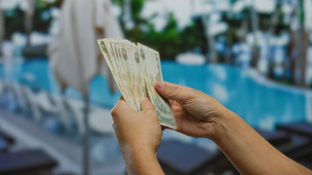 hands holding uae dirhams outdoors near luxurious poolside at a