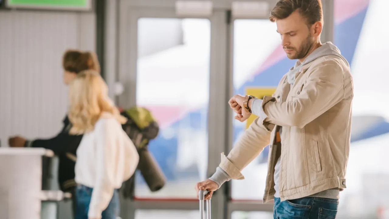 young man with suitcase checking wristwatch in airport