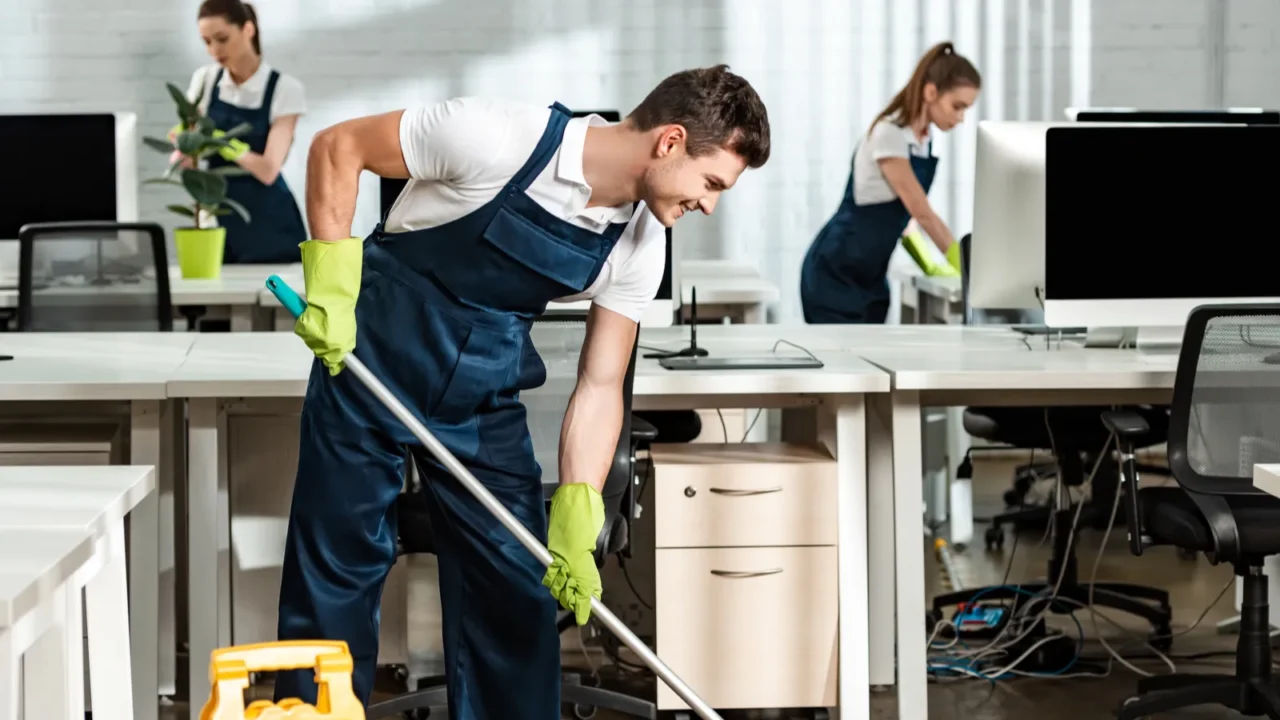 young smiling cleaner washing floor with mop in modern office