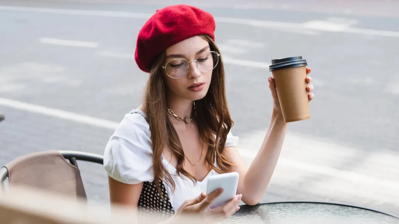 young woman in red beret and eyeglasses holding paper cup
