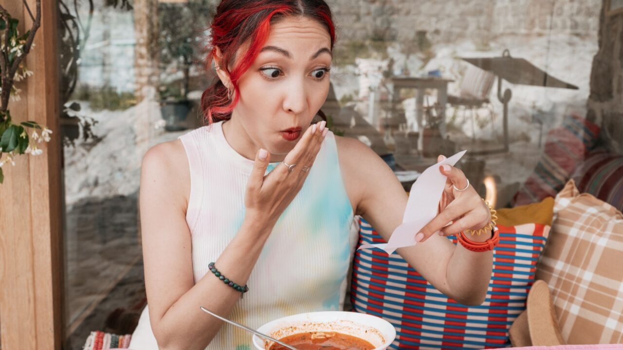 Shocked woman at a restaurant confronted with an unexpectedly expensive bill.