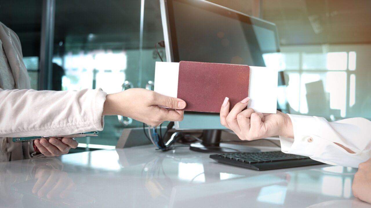 Hand of female traveler giving passport and boarding pass to passenger service agent staff for checking information at check in area airport terminal, travel on holiday or business trip transportation