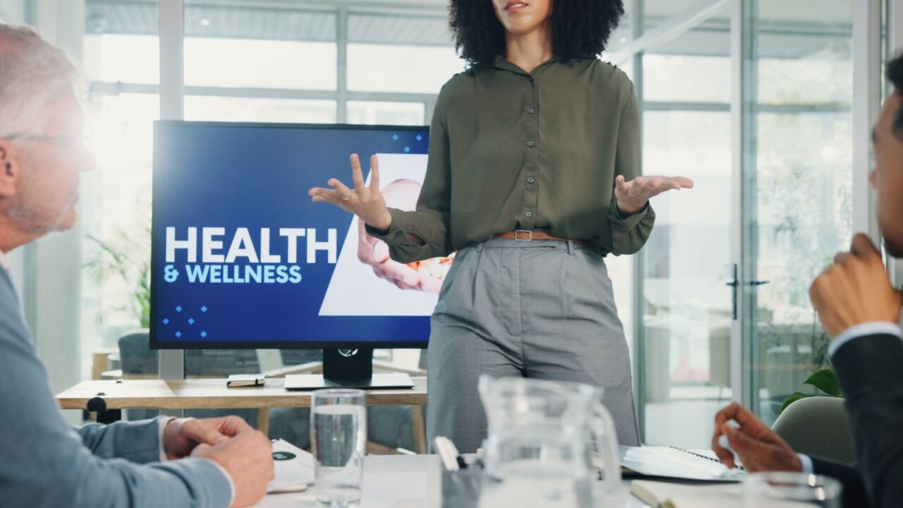 Presentation, health and wellness with screen at office, hands or talk with advice, info or pitch. Person, speaker and audience with monitor, discussion and employee wellbeing in boardroom at agency