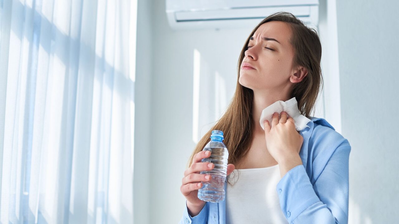 Sweating woman suffering from heat, hot weather and thirst wipes his neck with a napkin and cools down with air conditioning and cold refreshing water bottle. Refresh concept
